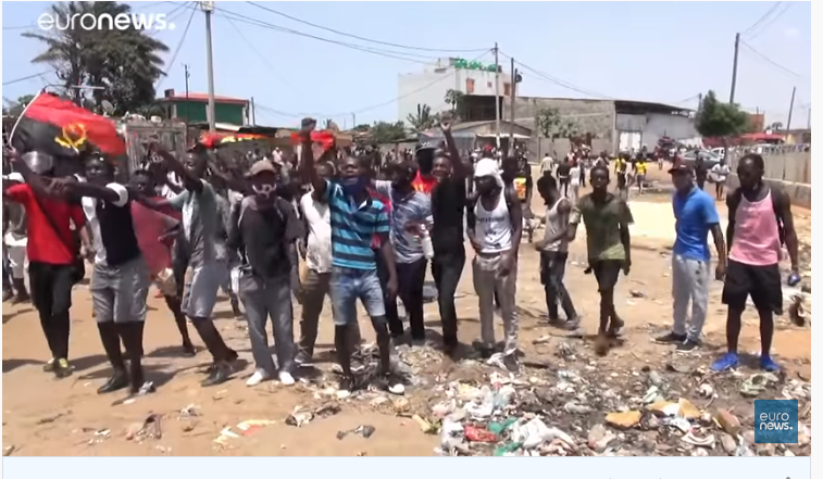 Un groupe de jeunes hommes portant le drapeau angolais marchent à Luanda, le poing levé, pour protester contre le gouvernement.
