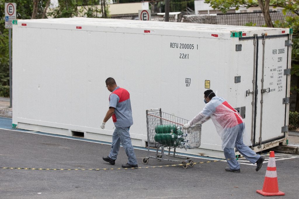 Перед великим білим контейнером два чоловіки штовхають візок із кисневими балонами.