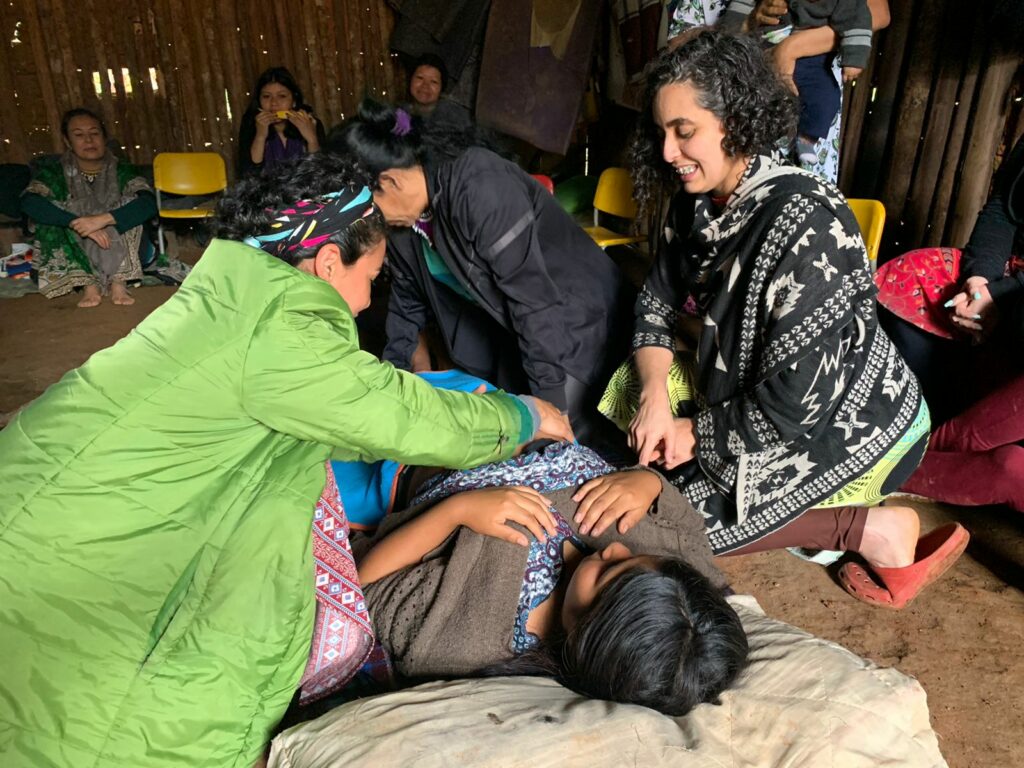 au premier plan, une femme enceinte allongée par terre, entourée de deux autres femmes qui veillent sur elle, lui mettent les mains sur le ventre, dans le fond d'autres femmes sont présentes assises